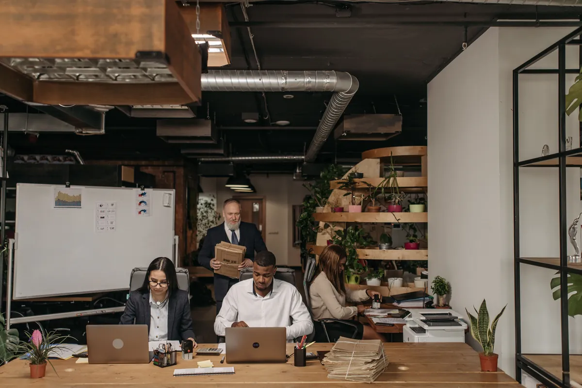 A group gathered around a wooden table in an industrial workspace, talking