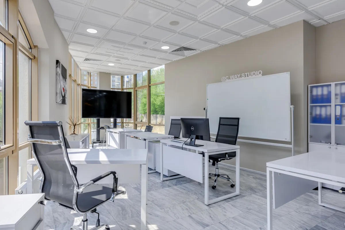 Bright open workspace with white desks, glass walls, and a whiteboard